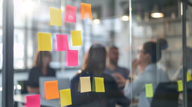 Business team brainstorming with sticky notes on a glass board while discussing ideas at a meeting table - Powered by Adobe