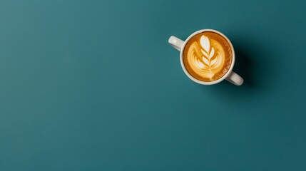   A cappuccino in a teacup, garnished with a leaf, against a teal green backdrop, as seen from above - obrazy, fototapety, plakaty