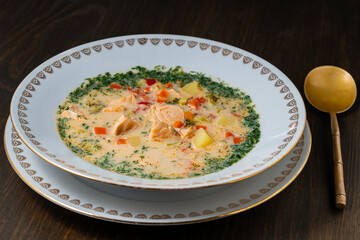 Fresh creamy salmon fish soup with potatoes, carrots, broccoli, peppers and onions in a ceramic plate on a wooden table, closeup. A delicious dinner consists of fish soup with salmon