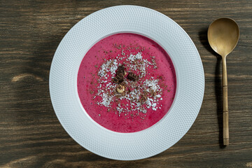 Sweet summer cherry soup in a white plate on a wooden background, closeup, top view. Hungarian cold red cherry soup with yogurt or cream, sprinkled with grated chocolate, powdered sugar and hazelnuts - 787811082