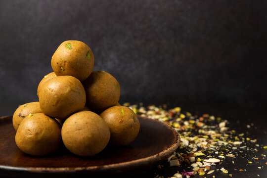 A wooden plate full of besan laddoos stacked. Dry fruits like badam (almonds), pista (pistachios)  studded.