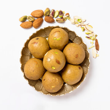 A brass bowl full of besan laddoos stacked. Dry fruits like badam (almonds), pista (pistachios)  studded.