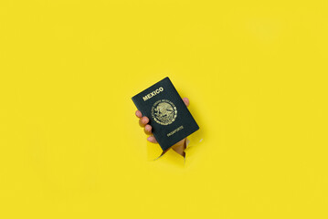 Female hand emerging from a hole in a torn paper background holding a Mexican passport.