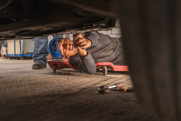 Mechanic under a car working leaning on wheeled platform