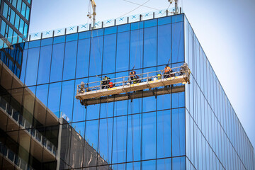 Far and corner shot of three window washers on a hanging scaffold on a commercial building with...
