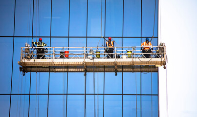 Straight on shot of three window washers on a hanging scaffold on a commercial building with blue...