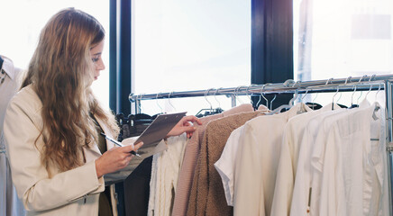 Check, clothes and employee with clipboard, boutique and small business of startup, retail and fashion. Store, woman and inventory of stock on hanger, writing and notes for inspection for shop