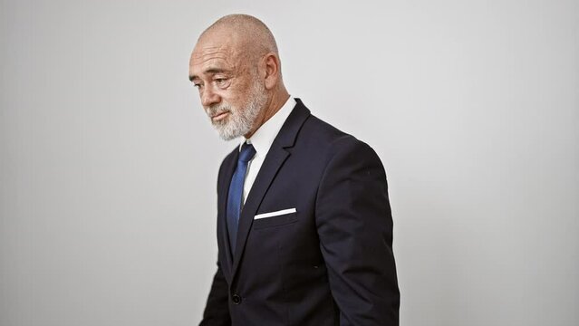 Mature bald man in suit stands against white isolated background expressing confident business demeanor.