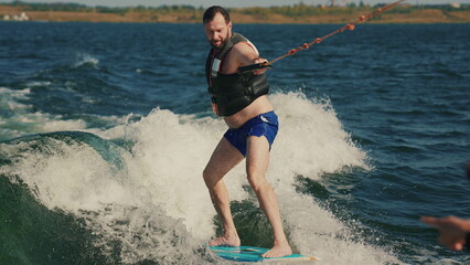 A man learns to wakesurf behind a boat. Fun on the water during the hot summer on the lake.