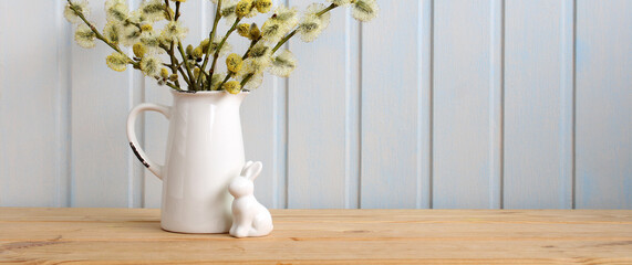 Easter banner with a rabbit figurine and a willow bouquet in a jug on the table. Easter background,...