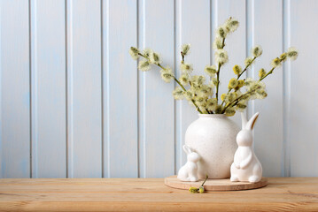 Easter bunny figurines and blooming fluffy willow branches on the table. Easter background, spring holiday backdrop. Copy space.