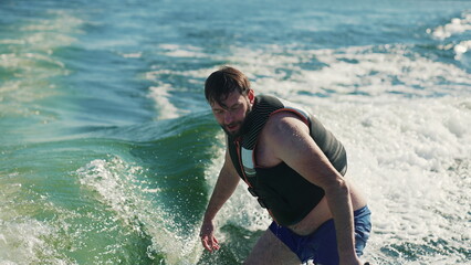 A man learns to wakesurf behind a boat. Fun on the water during the hot summer on the lake.