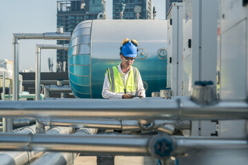 Serious engineer inspecting HVAC equipment with a tablet on a commercial building rooftop.