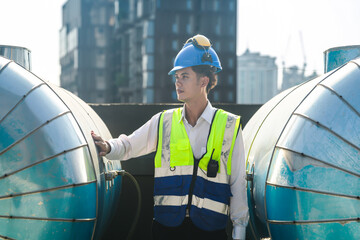 Engineer with safety gear inspects large industrial water tanks on a city rooftop against a skyline...