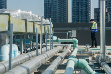 A professional engineer communicates via walkie-talkie on a building's rooftop, surrounded by piping and ductwork.