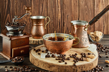 Splash Coffee in copper cup, vintage coffee grinder and jug with milk, lump sugar on wooden...