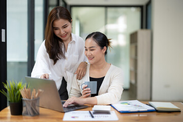 Two engaged colleagues collaborate on a project using a laptop in a bright office setting, discussing work with a smile.