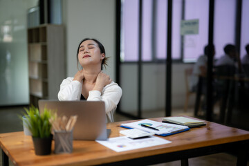 Businesswoman at her desk, thoughtfully assessing the information on her laptop screen, in a busy modern office environment.