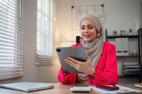 A female Muslim investor who trades in cryptocurrencies sits looking at stock charts and studying Bitcoin.
