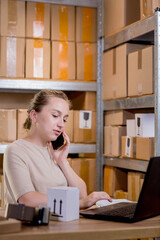 Portrait of woman entrepreneur holding smartphone and typing something at the keyboard while preparing information about parcel. Post service and small business concept.