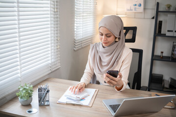 Muslim female entrepreneur wearing hijab sits working with laptop managing personal business in...