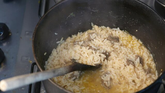 A pot of steaming rice on the stove. A wooden spoon in a pan. A steamy pot of cooked rice with pieces of cooked steak. A steaming beef risotto pot. Boiled rice, boiled meat (Arroz Carreteiro meal).