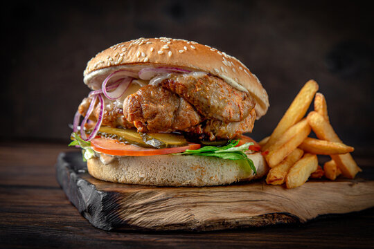 Burger with kebab meat, cheese, vegetables, sauce and iceberg lettuce. Juicy delicious hamburger on darkmood picture for restaurant decoration, poster. 
