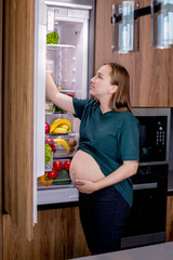 Young pregnant woman with an orange near the refrigerator at home. Healthy Eating