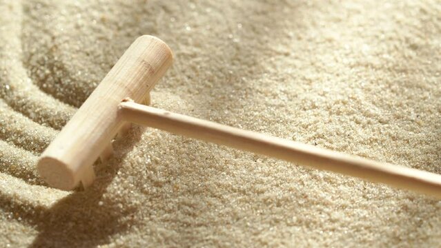 Close-up making sand zen garden using mini wooden rake with shadows and sunlight