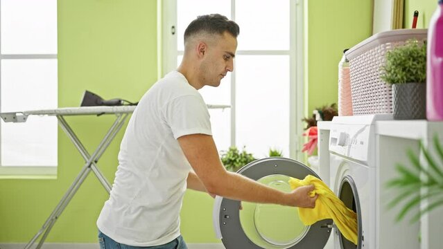 A young man does laundry indoors, depicting domestic life in a brightly colored room with a washing machine.