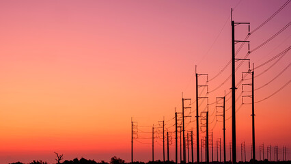 Silhouette two rows of electric poles with cable lines on curve country road against colorful...