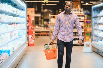 Portrait of smiling man at supermarket. Young african man with shopping basket in grocery store
