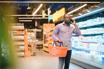 African American Man Talking On Cellphone Chatting While Shopping Groceries In Supermarket - obrazy, fototapety, plakaty