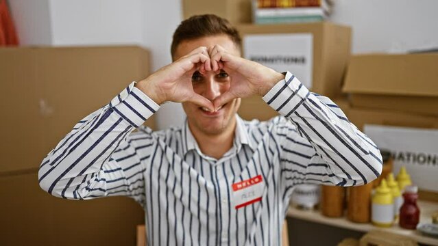 Smiling man making heart gesture in warehouse with donation boxes and condiments