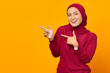 Cheerful asian woman pointing fingers to empty space on yellow b