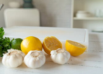 Empty white cutting board surrounded with ingrdients such as lemon, garlic and herbs in the kitchen