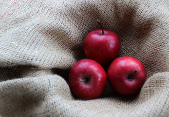 Three red apples in a fruit basket lined with burlap top view
