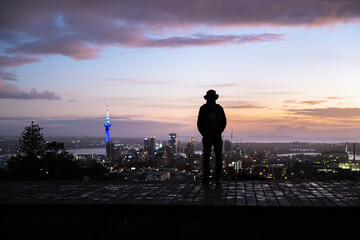Man in silhouette looking at the views of Sky Tower and cityscape. Mt Eden summit at dawn. Auckland.