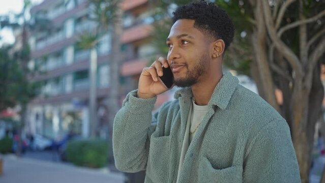 African american man in casual attire talks on a cellphone on a vibrant city street.