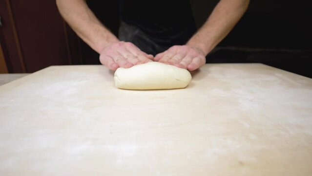 Rolling dough on floured countertop. Hands of a young man rolls out pastry dough on wooden pastry board