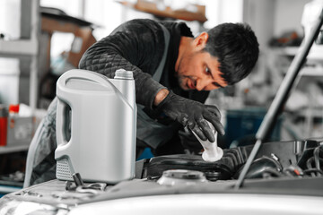 Close up of car service worker pouring new oil into car engine - 787964840