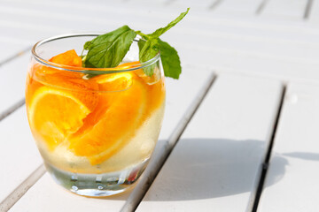 Citrus and mint leaves infused water, cocktail, lemonade in glass. Summer iced cold drink with lemon, orange, ice and mint on white wooden striped background, copy space, side view, hard shadows