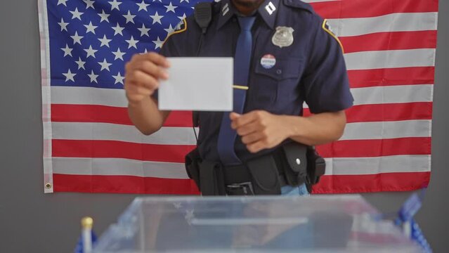An american male officer casts a ballot at a voting station with a usa flag backdrop.