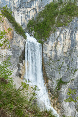 Boka waterfall in Slovenia, near Bovec. Easy trekking nature trail in the forest with the view of the immense waterfall overhanging the mountains visible from the road, long exposure photography.