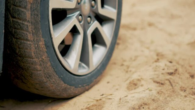 Car with chrome wheel rims drives along sandy road close up. Rotating tyre on dirty road. Automobile offroad