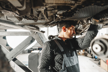 Workman mechanic working under car in auto repair shop - 787968048