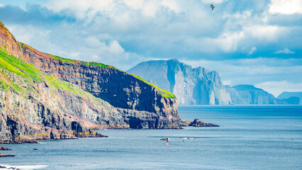 Mykines, Faroe Islands. Panoramic view of Mykines island, bird watching destination for puffins. Fjords landscape and seascape with flying puffins
