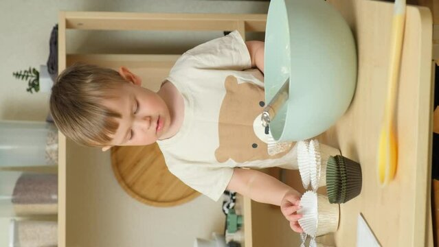 Little boy preparing to cook cupcakes, laying out muffin tins on table, vertical slow motion.