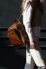 beautiful curly blond hair woman posing with a leather backpack