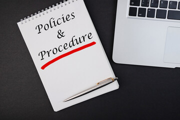The text, the inscription, the phrase Policies and Procedure is written in a notebook that lies on a dark table with a laptop and pen. Business concept